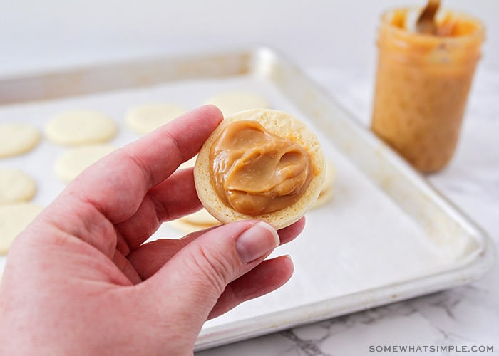 a hand holding a layer of cookie with dulce de leche spread on it